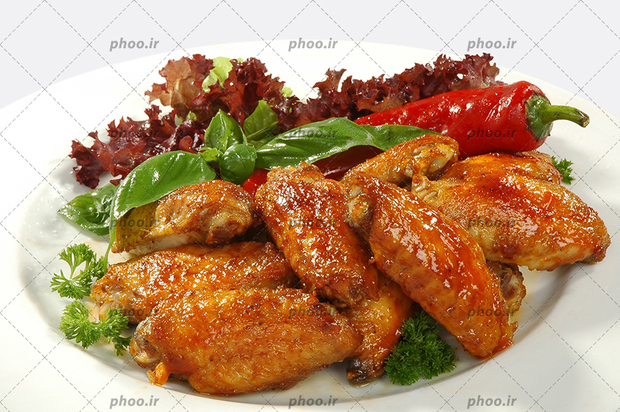عکس با کیفیت بال مرغ سوخاری شده در کنار سبزیجات و فلفل قرمز داخل ظرف چینی سفید