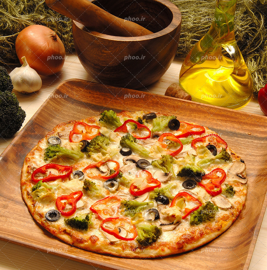 عکس با کیفیت پیتزا سبزیجات در سینی چوبی در کنار شیشه روغن زیتون و سیر و پیاز و هاون چوبی