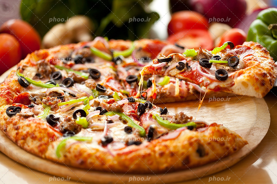 عکس با کیفیت در حال برداشتن یک اسلایس پیتزا سبزیجات از داخل ظرف چوبی و در اطراف آن گوجه ها و سبزی جات است