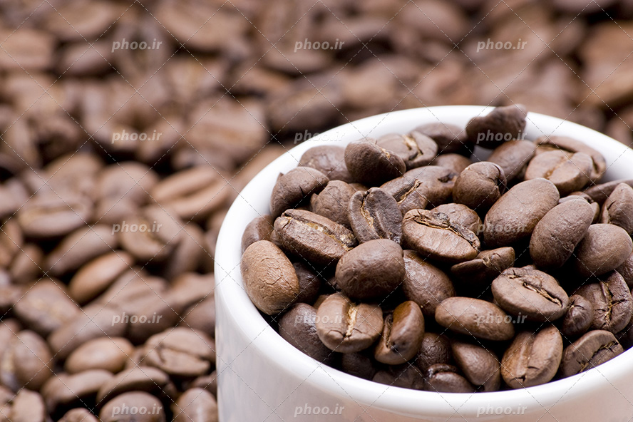 عکس با کیفیت دانه های قهوه داخل فنجان سفید و فنجان غرق در دانه های قهوه تازه