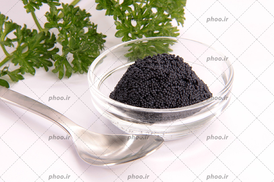 عکس با کیفیت خاویار سیاه در پیاله بلوری در کنار قاشق نقره ای و گیاه دارویی