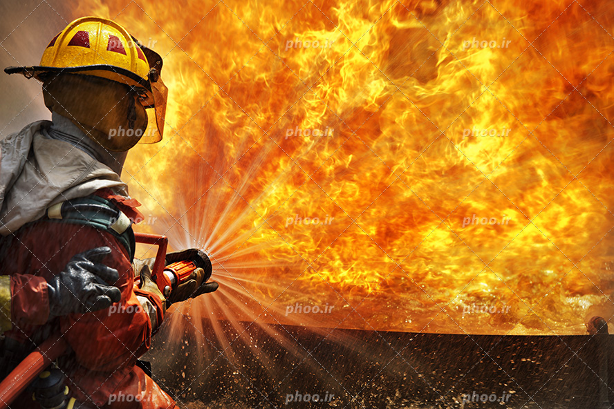 عکس با کیفیت آتش نشان در حال خاموش کردن آتش با کمک شلنگ آب ماشین آتش نشانی
