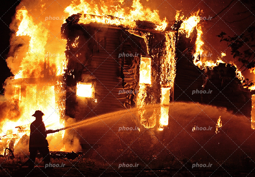 عکس با کیفیت آتش نشان در حال خاموش کردن خانه آتش گرفته با کمک شلنگ ماشین آتش نشانی