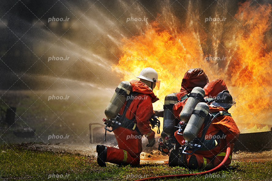 عکس با کیفیت آتش نشان ها در حال خاموش کردن شعله های آتش به کمک شلنگ ماشین آتش نشانی
