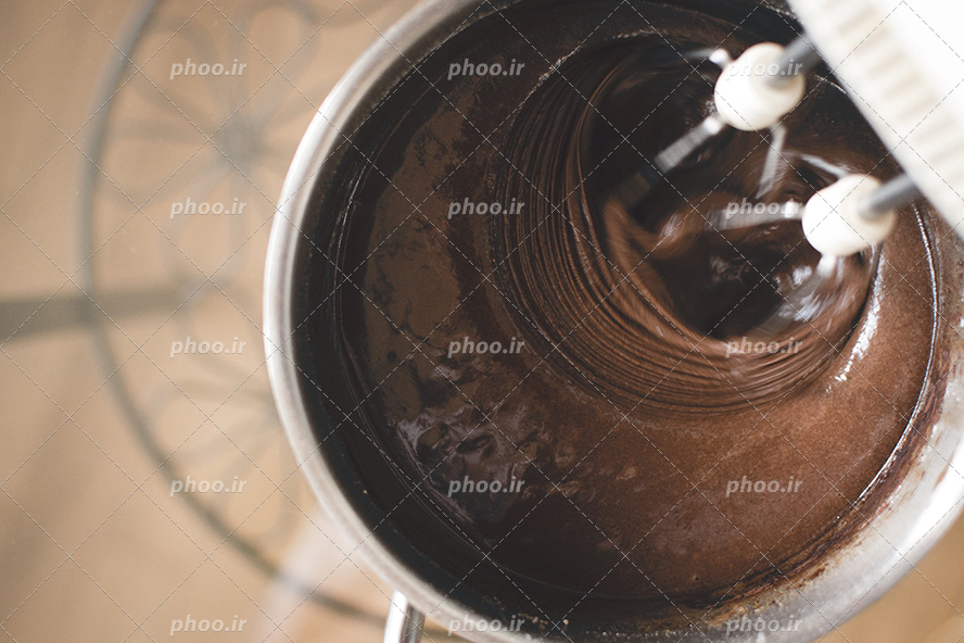 عکس با کیفیت همزن در حال هم زدن مواد کیک شکلاتی در ظرف استیل