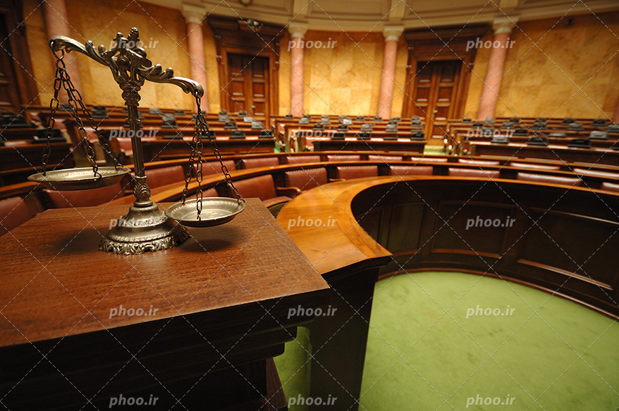 عکس با کیفیت دادگاه بزرگ با صندلی ها و میز های چوبی و ترازوی عدالت بر روی میز