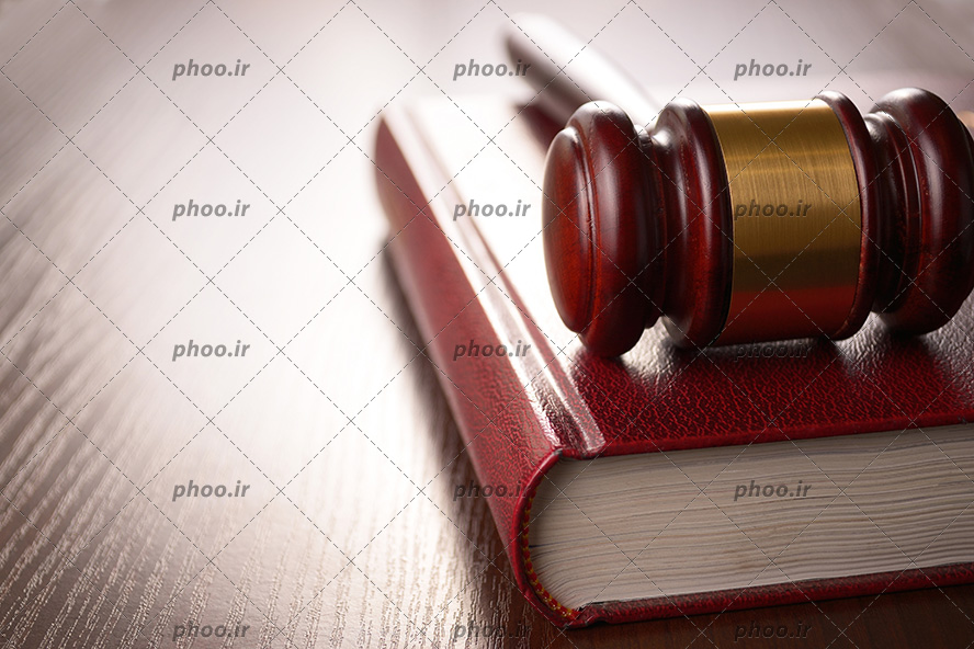 عکس با کیفیت چکش عدالت بر روی کتاب قانون و بر روی میز چوبی از نمای نزدیک