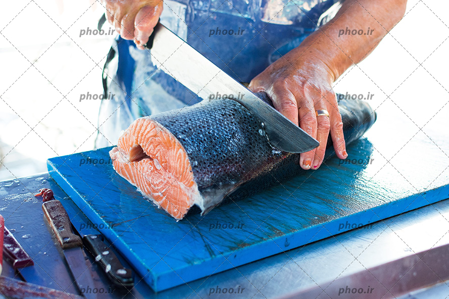 عکس با کیفیت ماهی فروش در حال قطعه قطعه کردن ماهی بزرگ با ساطور