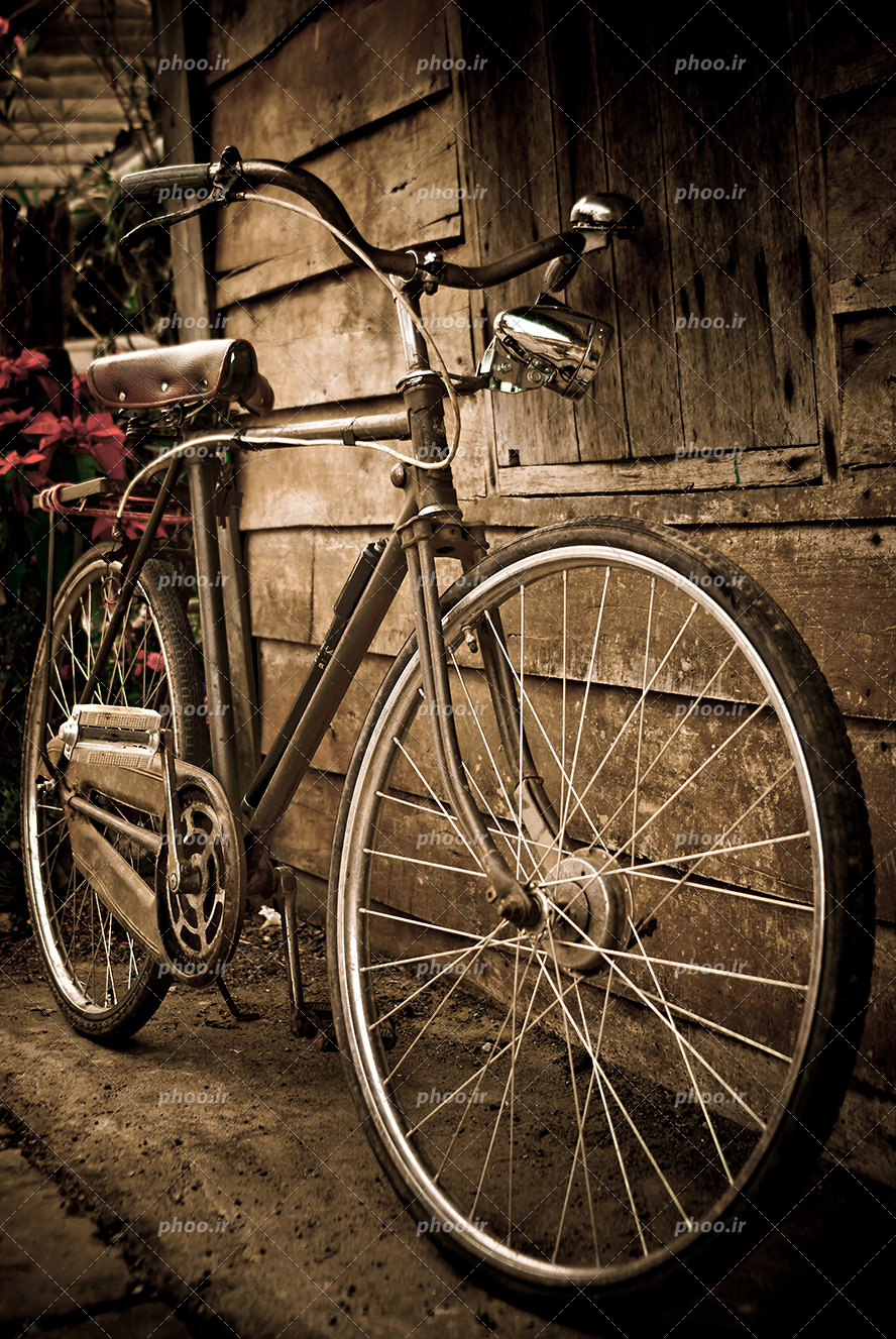 عکس با کیفیت دوچرخه ی قدیمی پارک شده در کنار خانه چوبی از نمای نزدیک