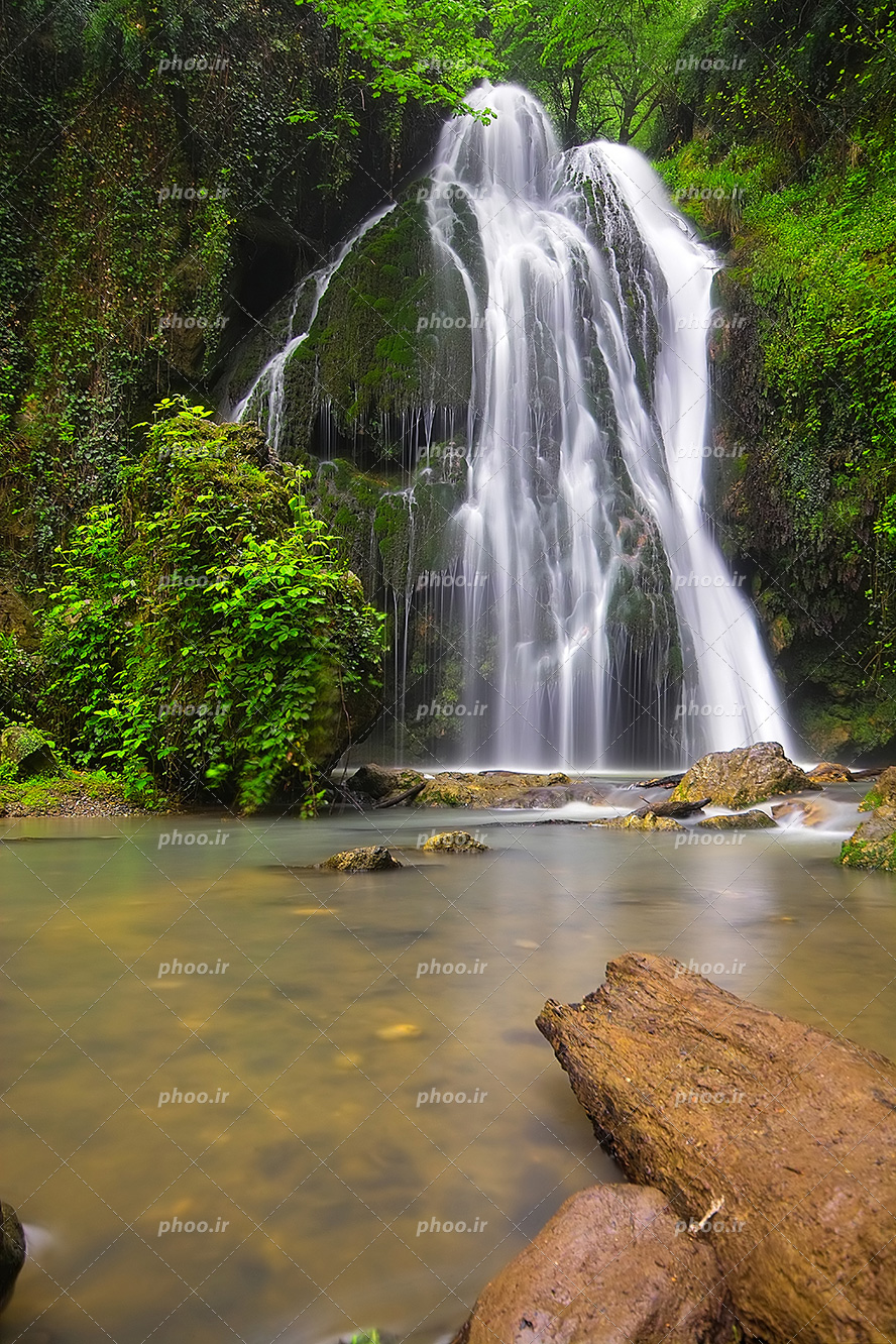عکس با کیفیت آبشار و آب های زلال و جنگل با درختان سبز و تخته سنگ ها داخل رودخانه