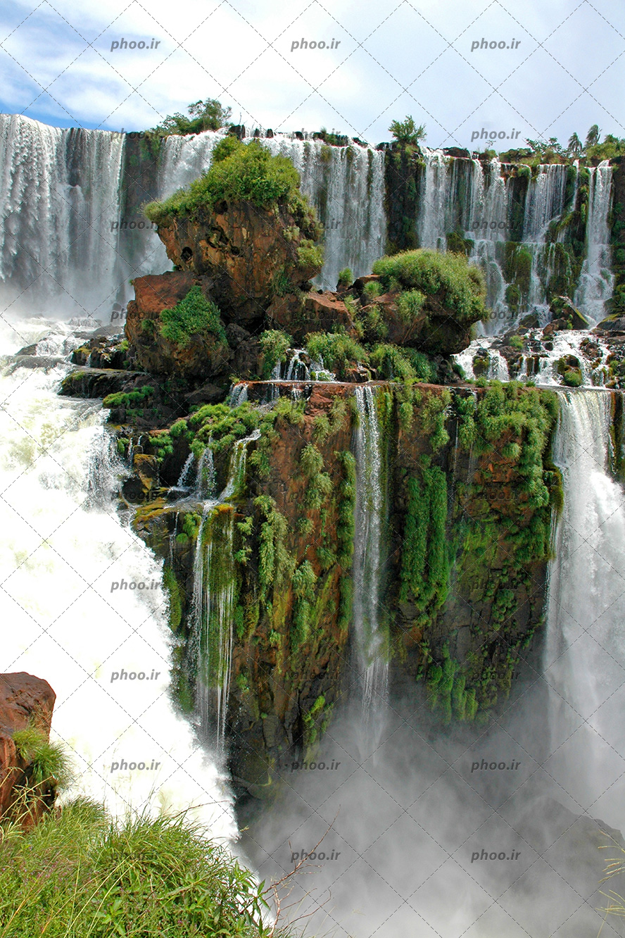 عکس با کیفیت روییدن گیاه بر روی تخته سنگ ها و کوه ها و آبشار بزرگ جاری شده از کوه