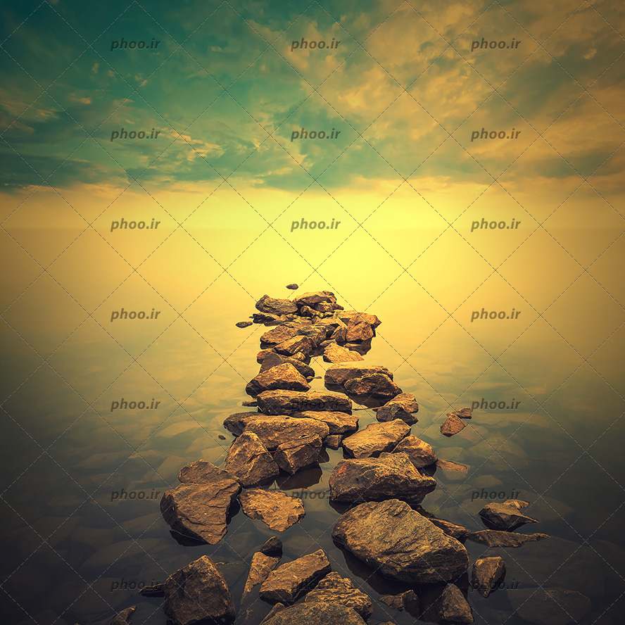 عکس با کیفیت تخته سنگ ها داخل آب در کنار یکدیگر به شکل پل و آسمان در حال غروب