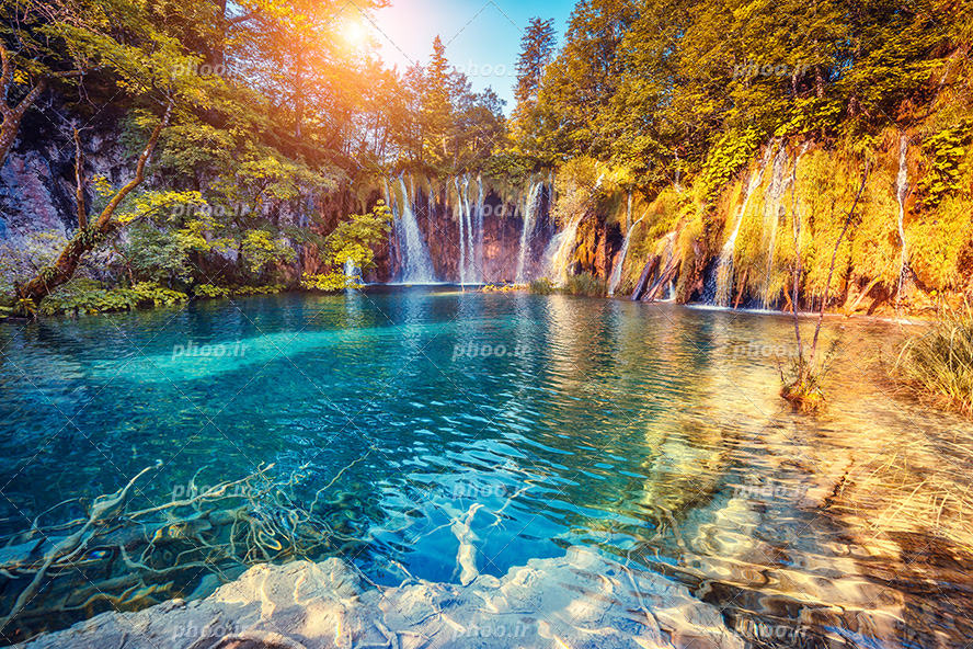 عکس با کیفیت دریاچه با آب شفاف و آبشار های جاری شده از کوه و درختان سرسبز بر روی کوه ها