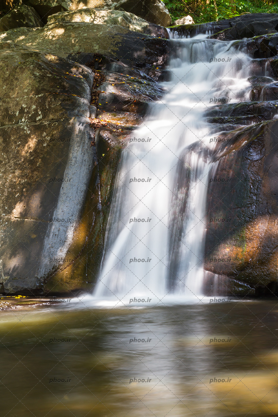 عکس با کیفیت آبشار آرام منتهی به دریاچه و تخته سنگ های بزرگ در اطراف