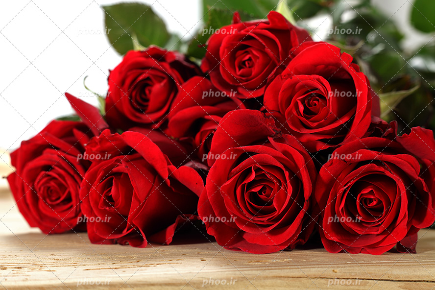 عکس با کیفیت دسته گل رز های قرمز بر روی میز چوبی