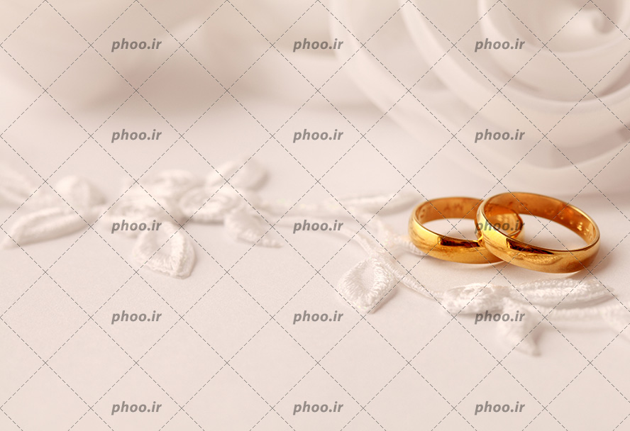عکس با کیفیت قسمتی از لباس عروس گلدوزی شده با نخ سفید و دو حلقه ازدواج بر روی پارچه از نمای نزدیک