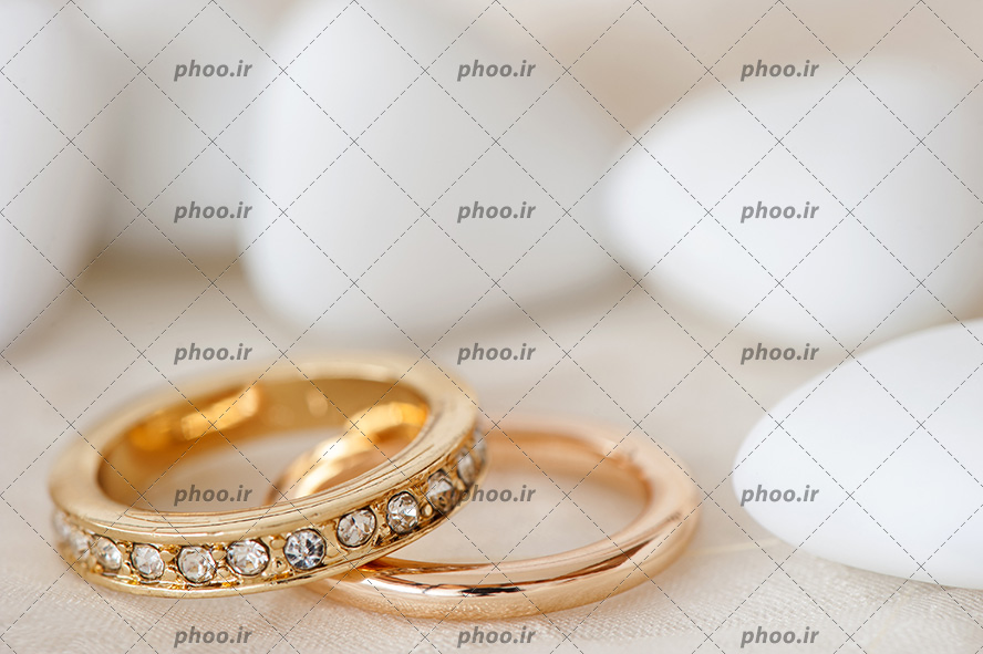 عکس با کیفیت یک حلقه طلایی تزئین شده با نگین های براق در کنار حلقه ساده
