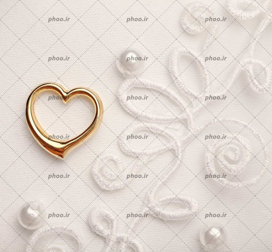 عکس با کیفیت حلقه طلایی به شکل قلب روی پارچه ی گلدوزی شده به رنگ سفید