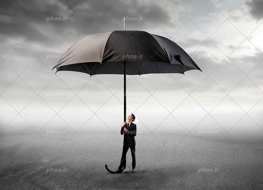 عکس با کیفیت آدم کوچک با کت و شلوار مشکی ایستاده بر روی ماسه ها و چتر بزرگ مشکی در دست