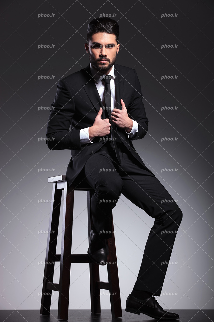عکس با کیفیت مرد با کت و شلوار مشکی نشسته بر روی صندلی چوبی