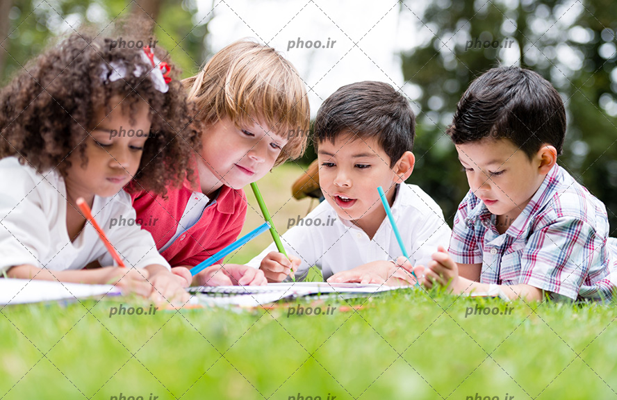 عکس با کیفیت کودکان نشسته در چمن های سرسبز و در حال نوشتن تکالیف خود