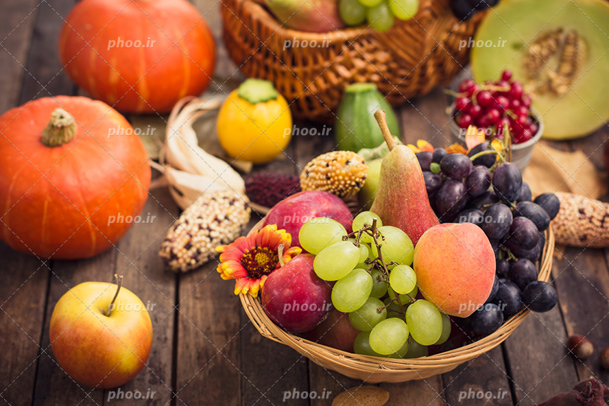 عکس با کیفیت ظرف حصیری پر شده از میوه های تازه مثل گلابی و انگور و شلیل در کنار کدو نارنجی و طالبی