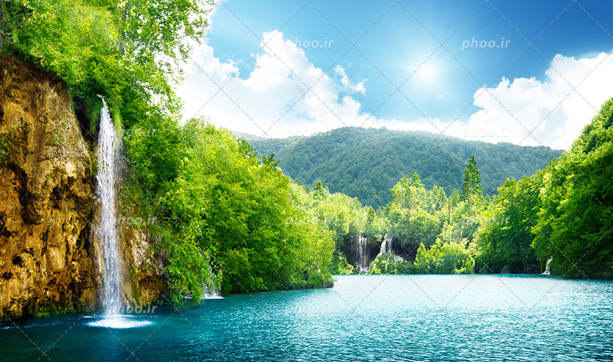 عکس با کیفیت طبیعت سرسبز با آبشار زیبا جاری شده از صخره بزرگ و دریاچه آرام با آب های زلال