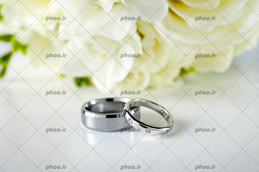 عکس با کیفیت انگشتر ست زنانه و مردانه در به رنگ نقره ای در کنار دسته گل عروس از نمای نزدیک