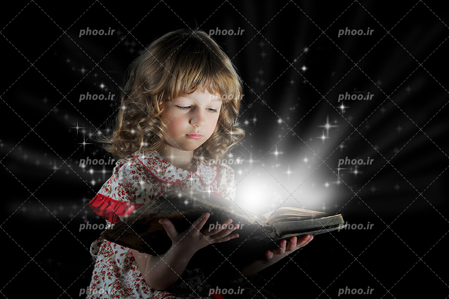 عکس با کیفیت کودک با لباس گلدار و موهای زیبا در حال خواندن کتاب نورانی در تاریکی