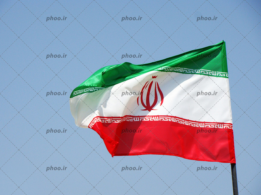 عکس با کیفیت پرچم ایران در آسمان آبی در حال تکان خوردن بر اثر وزش باد