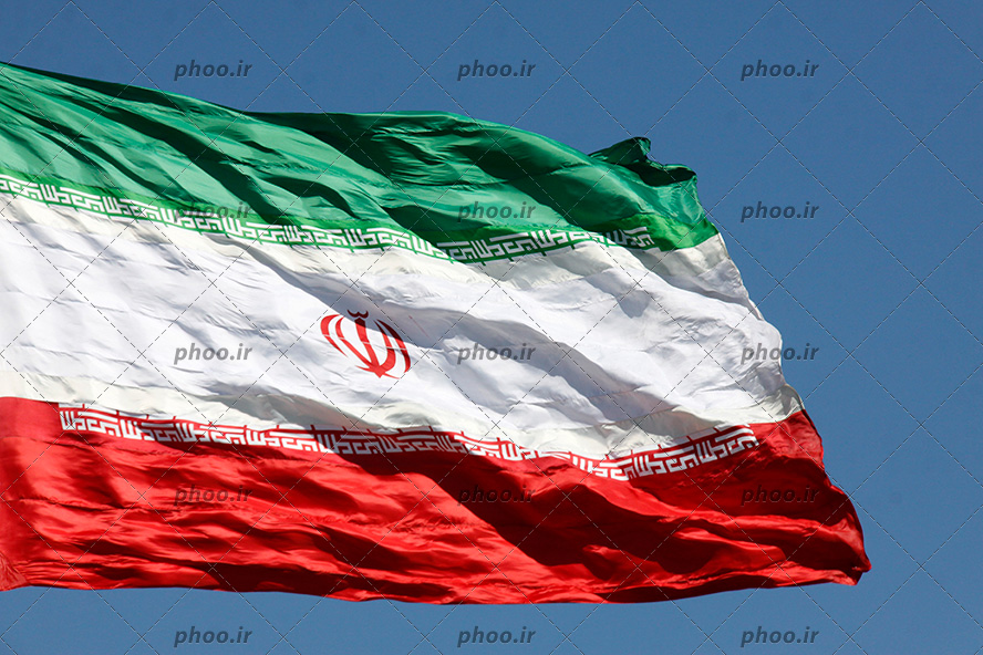 عکس با کیفیت پرچم با شکوه و زیبا ایران در آسمان آبی و چین خوردن پرچم به دلیل وزش باد