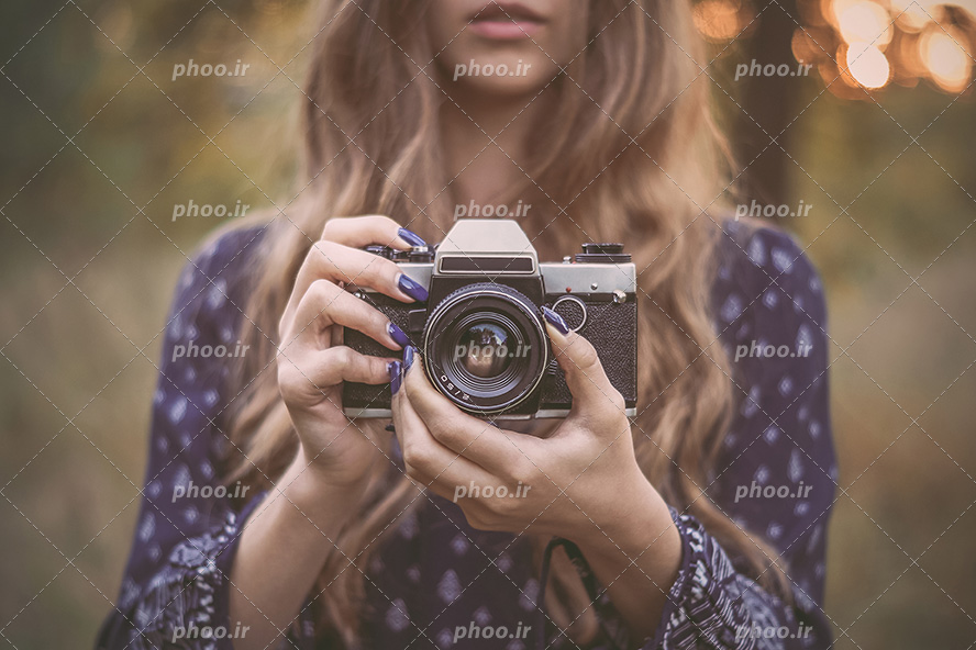 عکس با کیفیت دختر با موهای بلوند در حال تنظیم کردن فوکوس دوربین و عکاسی در طبیعت