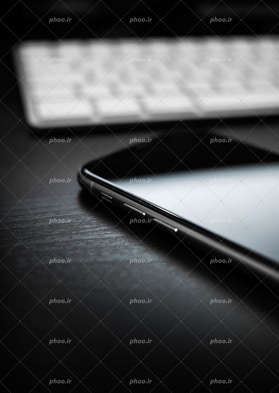عکس با کیفیت تلفن همراه هوشمند بر روی میز چوبی و تصویر مات شده کیبورد سفید در گوشه ای از تصویر