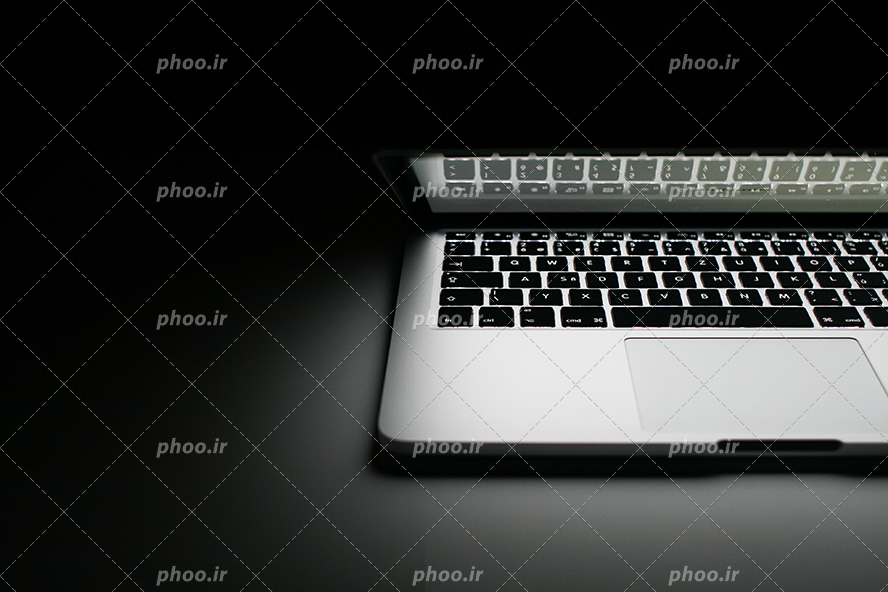 عکس با کیفیت فضای تاریک و لپ تاپ نیمه باز با نور سفید رنگ افتاده بر صفحه کلید لپ تاپ