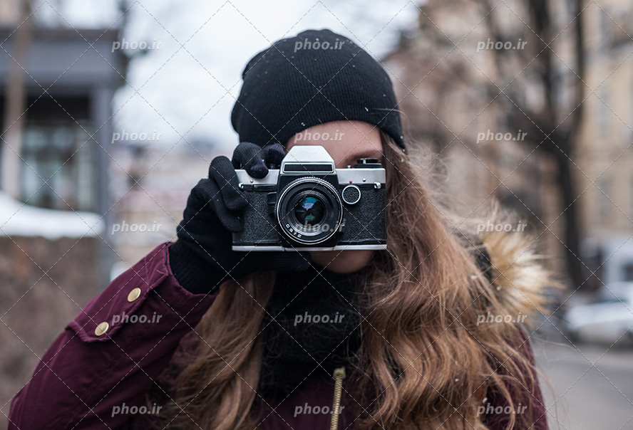 عکس با کیفیت زن با لباس گرم و دوربین عکاسی در مقابل صورتش در حال عکس گرفتن