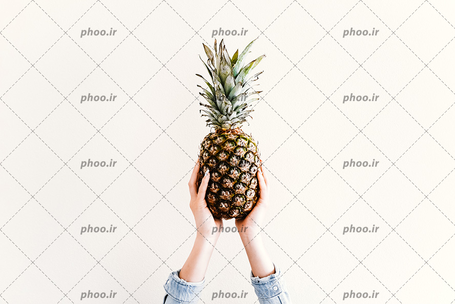 عکس با کیفیت آناناس در دست زن در پس زمینه کرمی