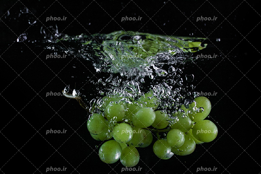 عکس با کیفیت خوشه انگور سبز در حال غرق شدن در آب و پس زمینه مشکی