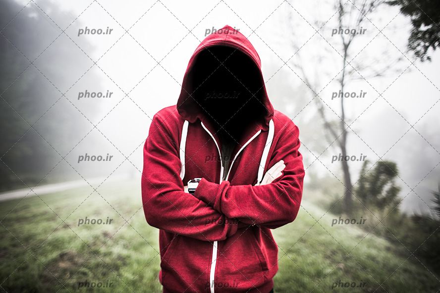 عکس با کیفیت مرد ایستاده در طبیعت با سویشرت قرمز و چهره ی سیاه شده