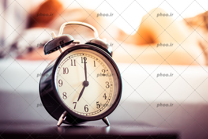 عکس با کیفیت ساعت رومیزی زنگ دار مشکی رنگ بر روی میز