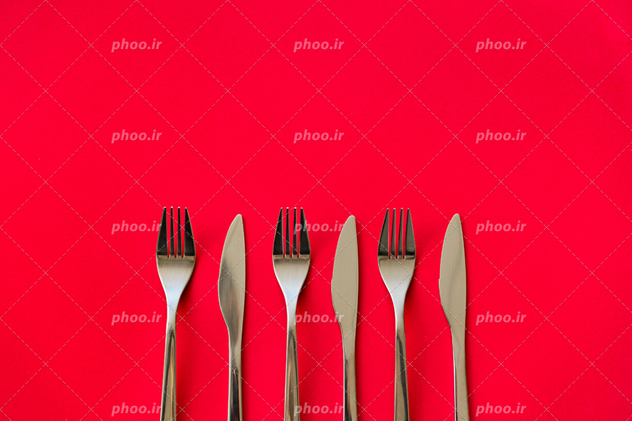 عکس با کیفیت سه چنگال و سه چاقو چیده شده در کنار یکدیگر در پس زمینه قرمز