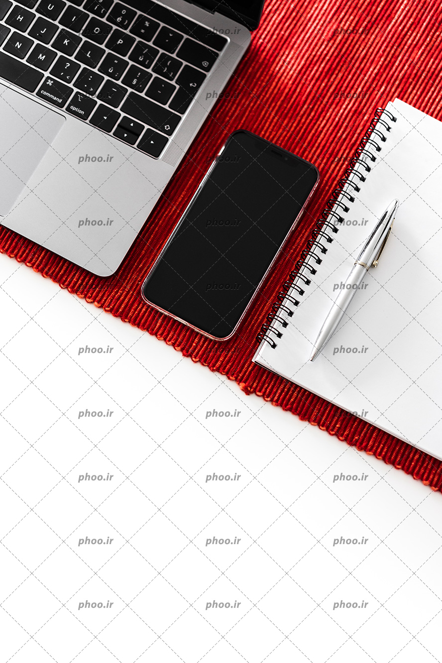 عکس با کیفیت تلفن همراه مشکی در کنار دفتر فنری و لپ تاپ بر روی پارچه کبریتی قرمز رنگ