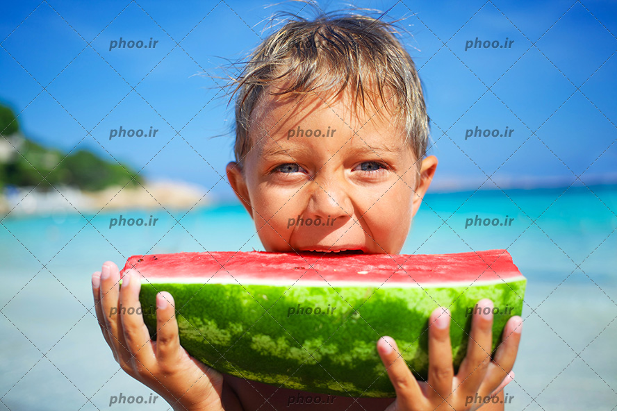 عکس با کیفیت پسر بچه ای در کنار دریا در حال خوردن هندوانه