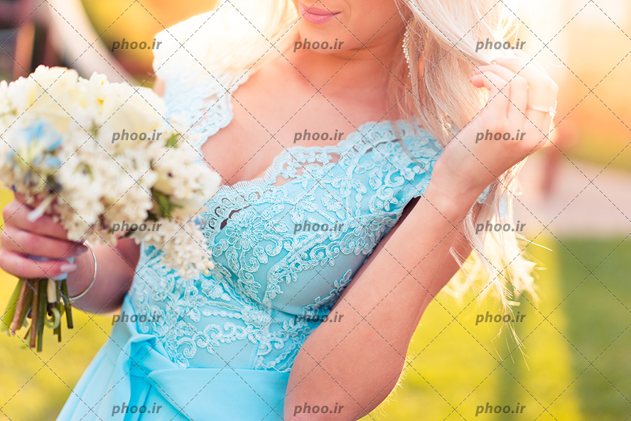 عکس با کیفیت عروس زیبا با لباس عقد آبی و موهای بلوند و دسته گلی در دست او در طبیعت