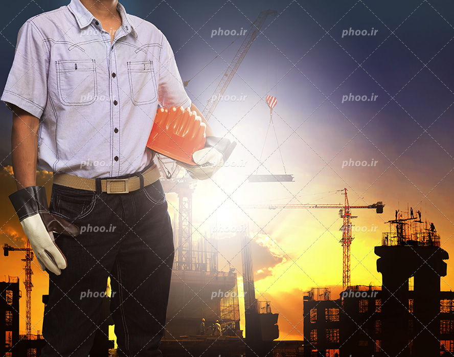 عکس با کیفیت مرد ایستاده پشت به ساختمان های نیم ساز و کلاه ایمنی در دستان او