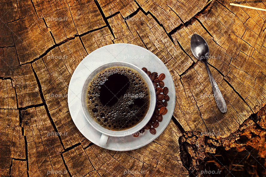 عکس با کیفیت فنجان اسپرسو و دانه های قهوه در کنار فنجان و قاشق در کنار آنها بر روی میز چوبی