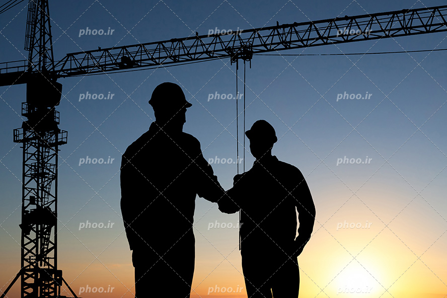 عکس با کیفیت دو مهندس عمران در حال دست دادن به یکدیگر و تاور کرین در کنار آنها و غروب آفتاب