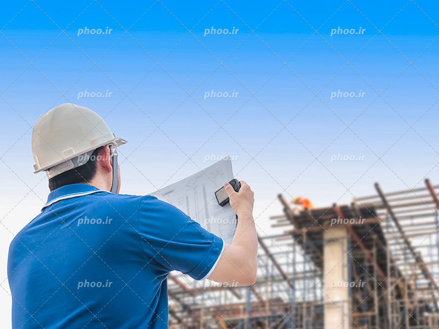 عکس با کیفیت دوربین و نقشه ی ساختمان در دستان او در مقابل ساختمان نیمه ساز و کلاه ایمنی بر سر او