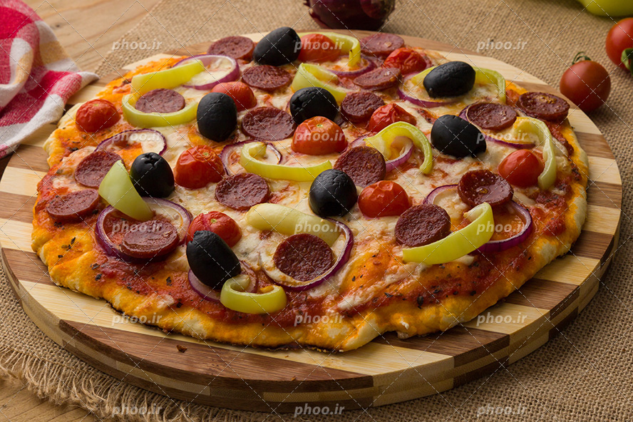 عکس با کیفیت پیتزای خوشمزه تزئین شده با زیتون سیاه و سوسیس ها و مقداری پیاز