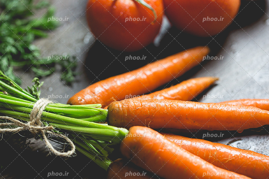 عکس با کیفیت هویچ های تازه و نارنجی دسته شده در کنار گوجه ها