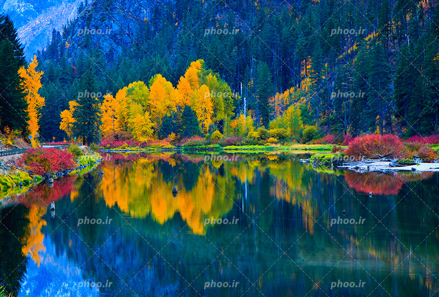 عکس با کیفیت زیبا و منحصربفرد درختان نارنجی و سبز و قرمز در اطراف دریاچه زیبا و کوه های پر شده از درخت